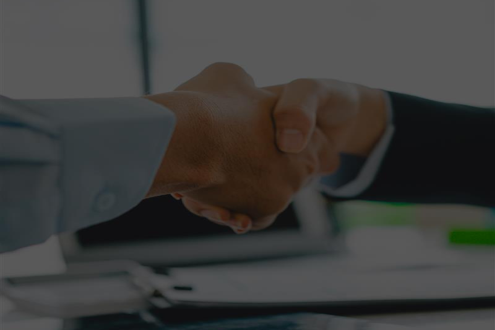 Two people shaking hands over a desk with documents.