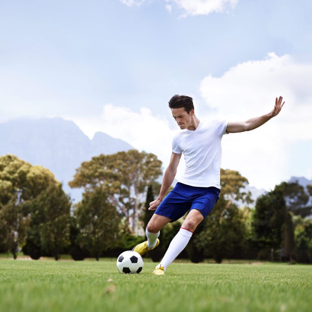 A man in white shirt kicking a soccer ball outdoors.